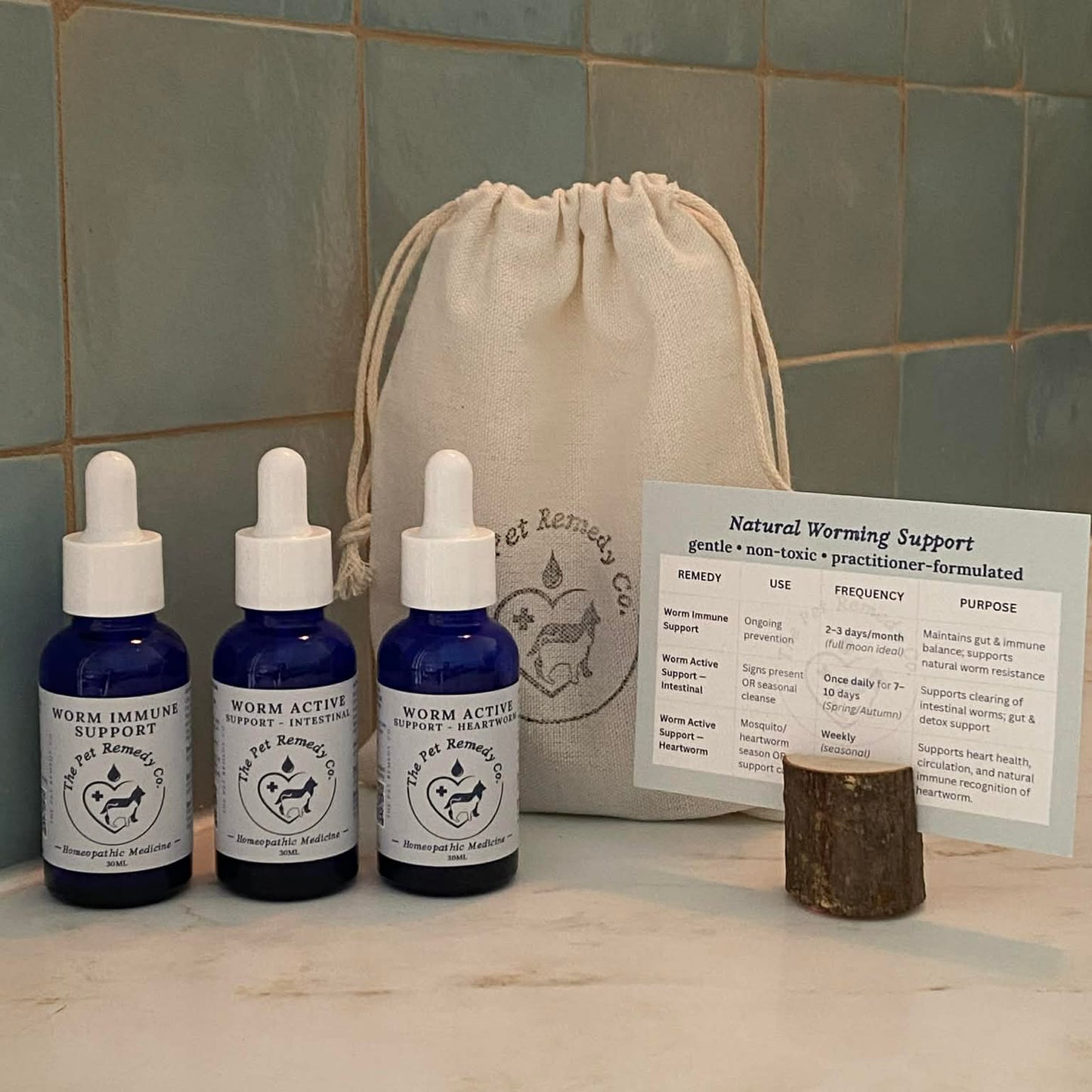 Three blue bottles with white droppers on a marble surface next to an information card and beige drawstring bag
