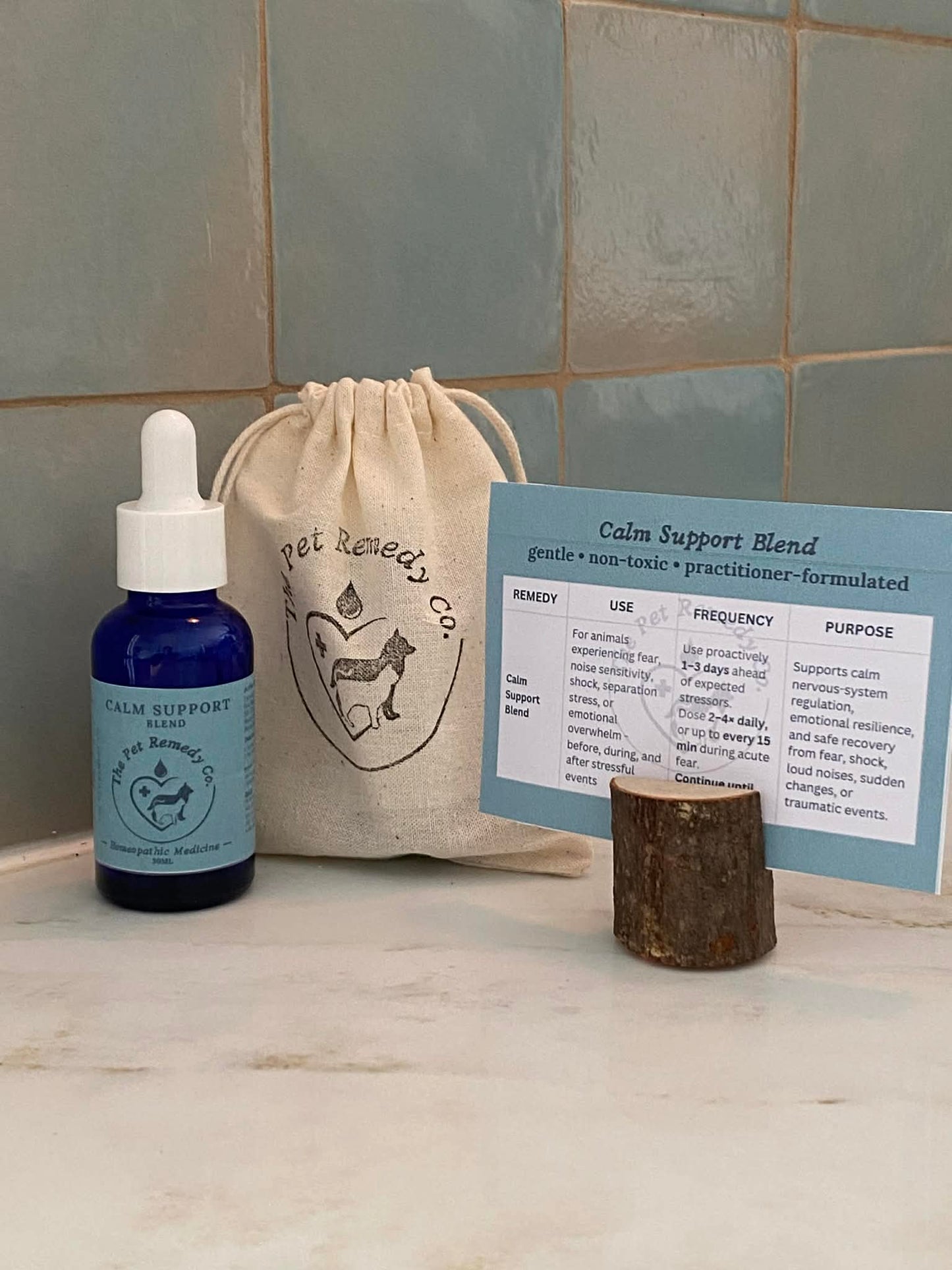 Pet remedy calm support bottle, drawstring bag, and information card on a tiled surface.